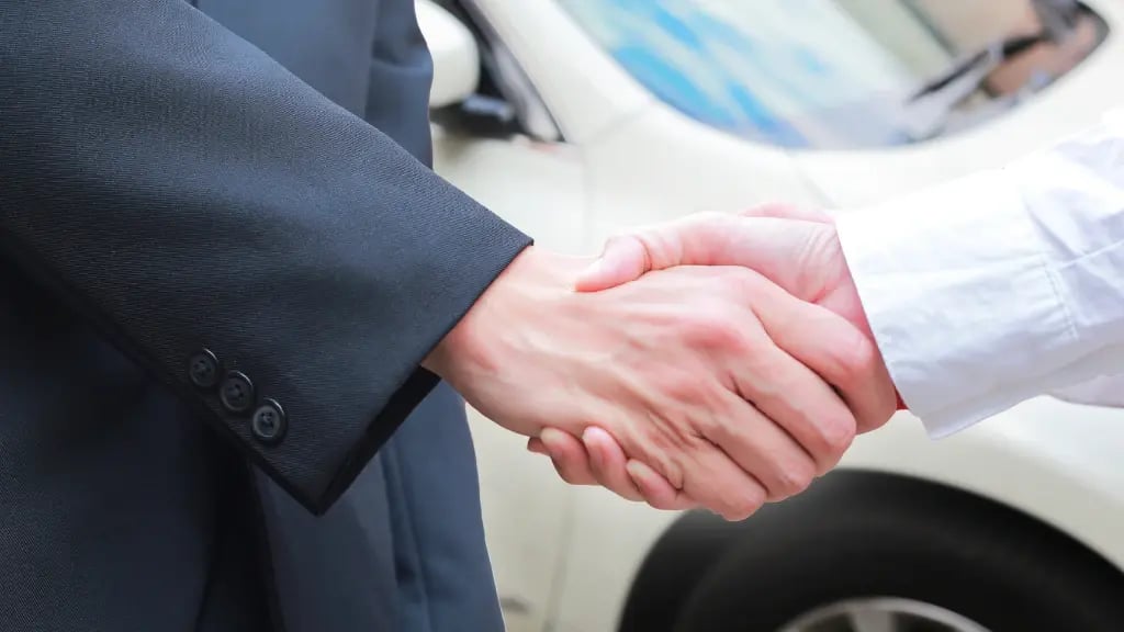 Zwei Menschen geben sich vor einem Auto die Hand